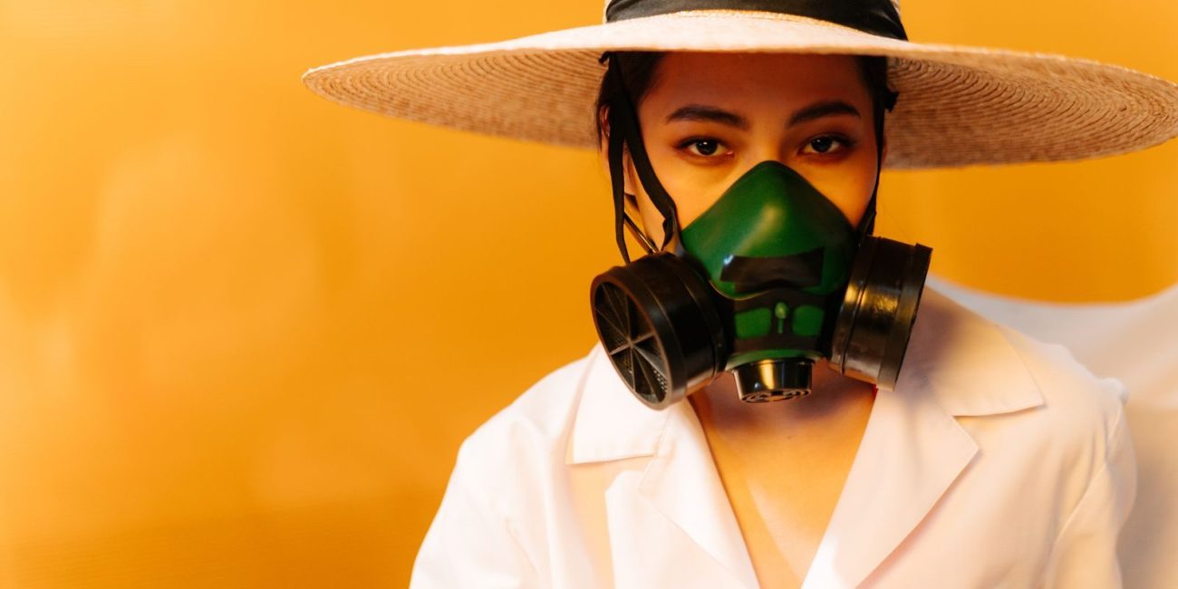 Conceptual portrait of a woman in safety gear with a straw hat and gas mask.