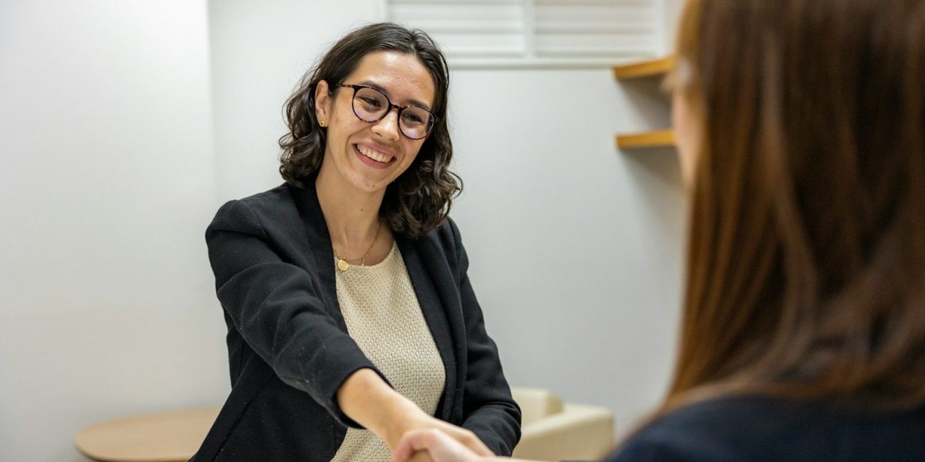 a woman shaking hands with another woman sitting at a table